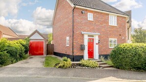 Una casa a due piani in mattoni con una porta rossa, un garage e un giardino curato.