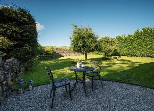 Une terrasse de jardin avec une table ronde, deux chaises et une petite table agrémentée d’une bougie et d’une bouteille.