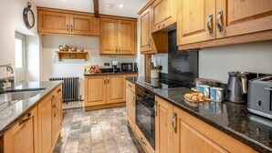 Une cuisine avec des meubles de rangement en bois, un plan de travail noir, une cuisinière, un four à micro-ondes et une bouilloire.