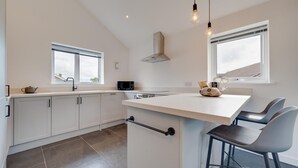 Una cocina moderna con armarios blancos, una isla central, taburetes de bar e iluminación colgante.
