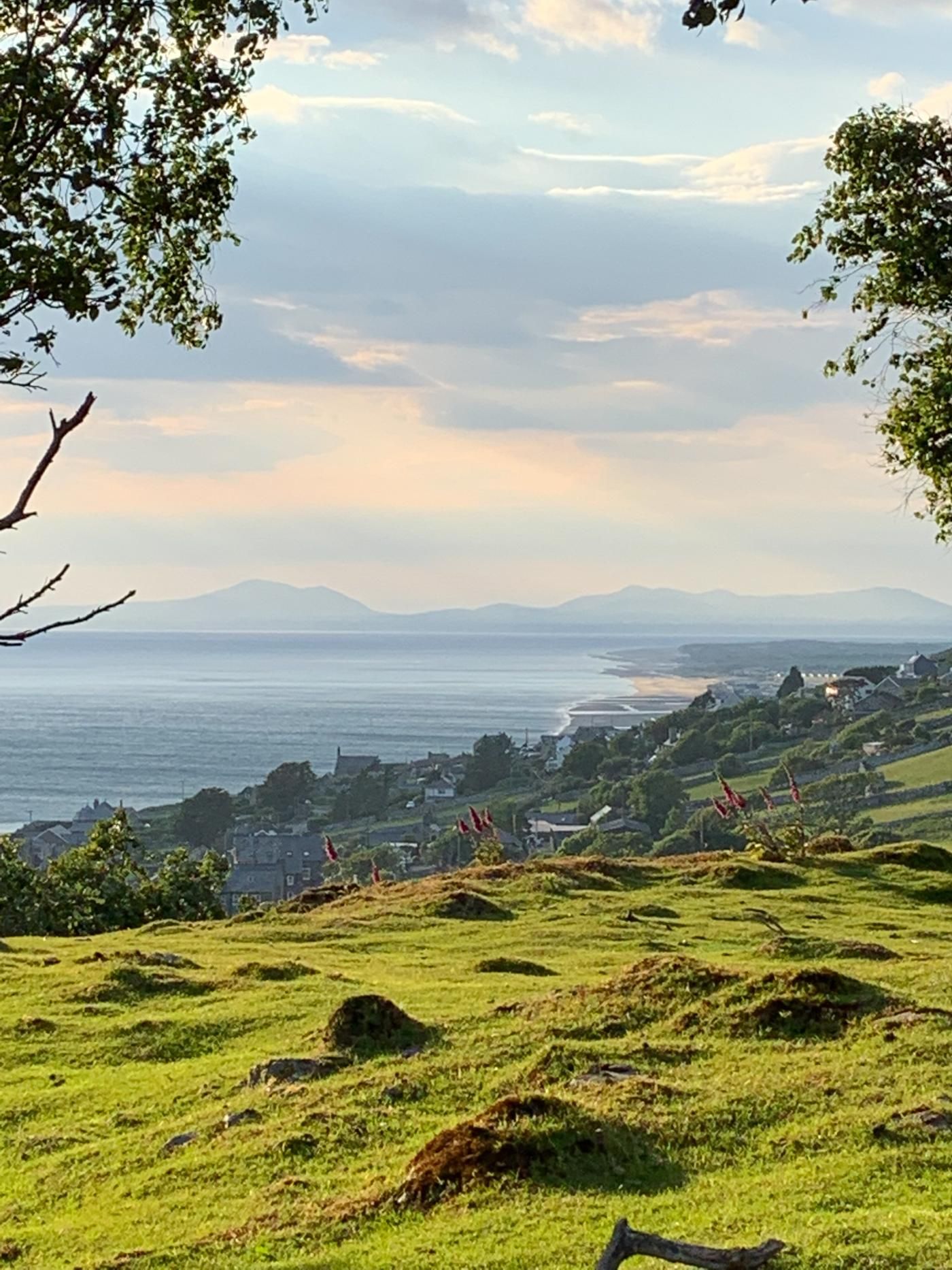 Un paysage côtier caractérisé par des collines douces, une vue sur la mer et une chaîne de montagnes lointaine.