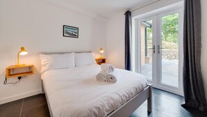 Una habitación de hotel moderna con una cama grande, dos lámparas de noche, un cuadro en la pared y vistas a través de la puerta de cristal.