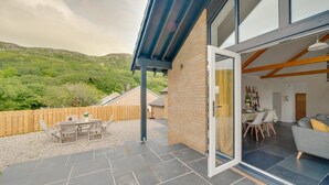 Una casa moderna con un patio, un comedor y vistas a colinas verdes.