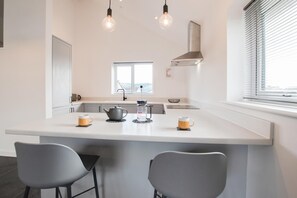 A modern kitchen with a central island, two bar stools, a kettle, and two mugs. - 3 Bed in Barmouth (oc-wah701) (Barmouth)