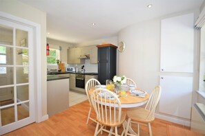 A compact kitchen with a dining area, featuring a round table with chairs, a microwave, and a stove. - 2 Bed in Little Petherick (oc-p00635) (Little Petherick)