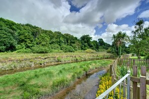 A natural landscape with a river, dense greenery, and a wooden fence. - 2 Bed in Little Petherick (oc-p00635) (Little Petherick)