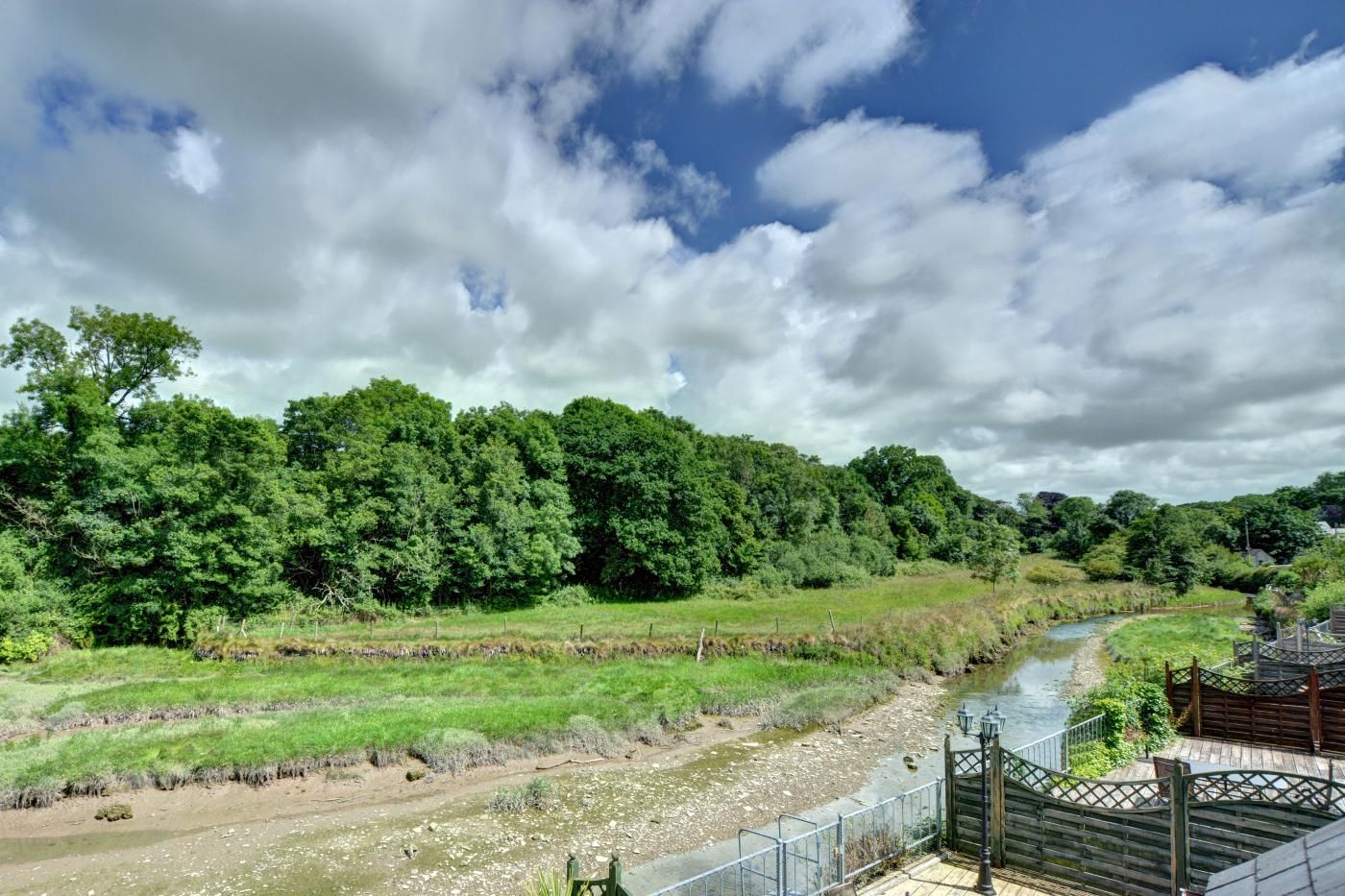 A river flowing through a forested area with a wooden bridge and a fence.
