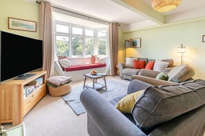 A living room with a sofa, a red bench, a television, and a window with curtains.