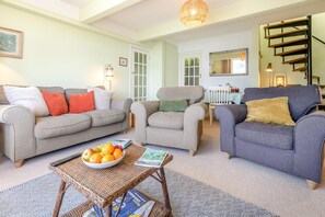 A living room with two sofas, a coffee table with magazines and fruit, and a staircase. - 2 Bed in Helford (oc-hcview) (Helford)