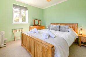 A bedroom with a wooden bed, a bedside table, a nightstand, a lamp, and a window with a view of trees.