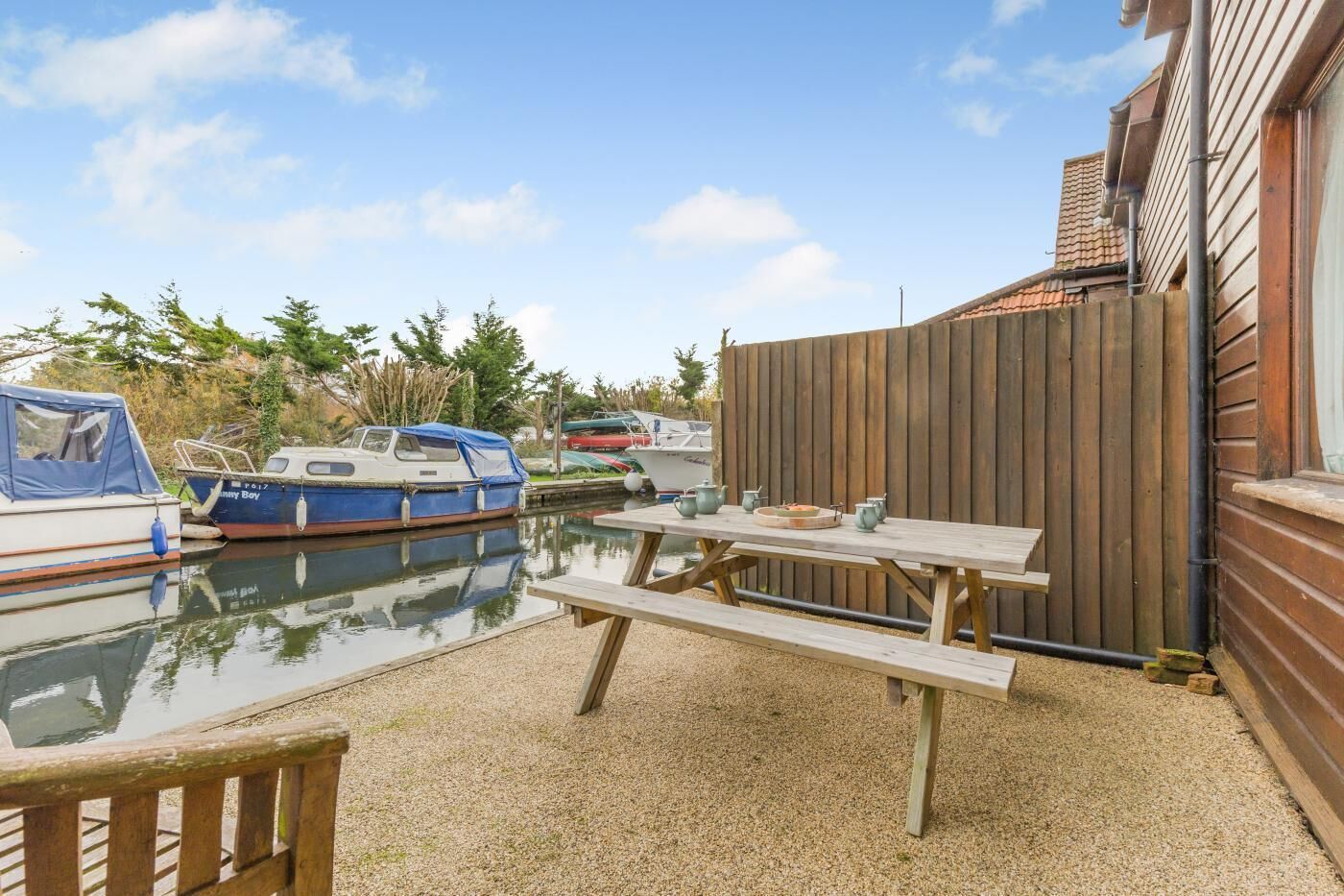 A wooden deck with a picnic table, boats docked in the background, and a wooden fence.