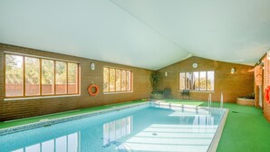 Una piscina interior con paredes de vidrio transparente, pared de ladrillo y suelo verde.