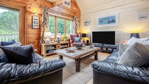 Un interior de cabaña acogedor con paredes de madera, un televisor grande y sofás de cuero.
