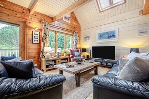 Un interior de cabaña acogedor con paredes de madera, un televisor grande y sofás de cuero.