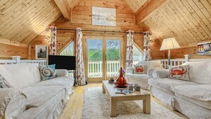 Un interior de cabaña acogedor con dos sofás blancos, una mesa de centro de madera y un televisor.