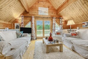 Un interior de cabaña acogedor con dos sofás blancos, una mesa de centro de madera y un televisor.