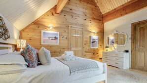 Un dormitorio con techo de madera, cama con ropa blanca, cómoda y espejo.