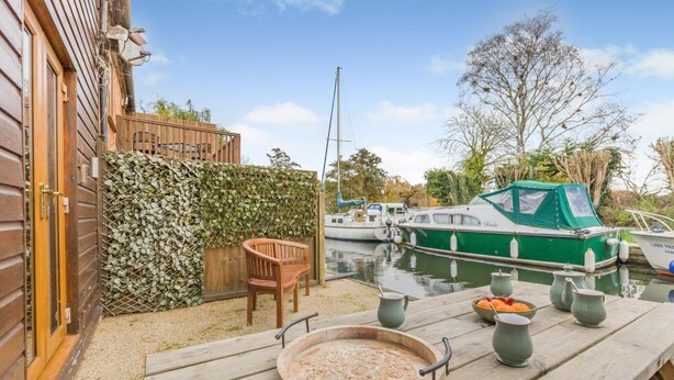A wooden deck with a table set for dining, a wooden chair, and a boat docked in the background. - 2 Bed in Smallburgh (oc-g33735) (Low Street)