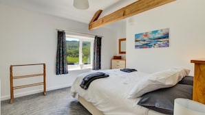 Ein Schlafzimmer mit einem Bett, einem Holzstuhl, einer Kommode, einem Fenster mit Vorhängen und einem Bild an der Wand.