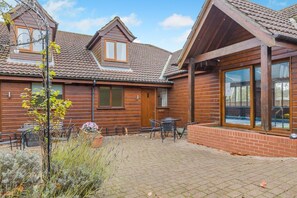 Eine Holzhütte mit Ziegeldach, einer Ziegelterrasse und Sitzgelegenheiten im Freien.