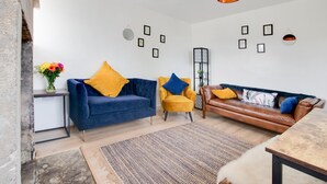 A modern living room with a blue sofa, a yellow armchair, and a brown leather sofa. There are framed pictures on the walls, a vase with flowers on a side table, and a hanging light fixture. - 2 Bed in Matlock (oc-dcbeau) (England)