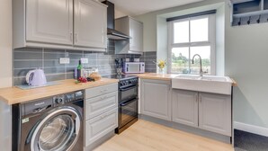 A modern kitchen with grey cabinets, a washing machine, a microwave, and a large window. - 2 Bed in Matlock (oc-dcbeau) (England)