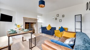 A modern living room with a fireplace, a sofa set, a dining table with plates and glasses, and a mounted TV. - 2 Bed in Matlock (oc-dcbeau) (England)
