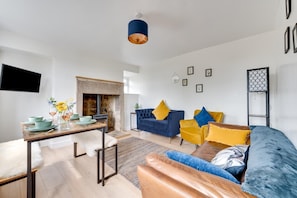 A modern living room with a fireplace, a sofa set, a dining table with plates and glasses, and a mounted TV. - 2 Bed in Matlock (oc-dcbeau) (England)
