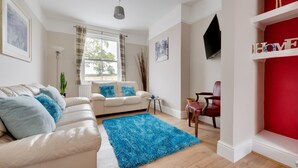 Ein Wohnzimmer mit einem beigefarbenen Sofa, einem blauen Teppich, einer roten Akzentwand und einem an der Wand befestigten Fernseher.
