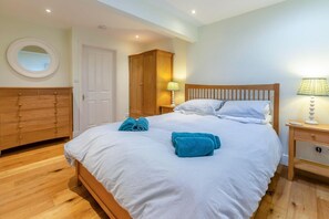 A bedroom with a bed, a wooden wardrobe, a round mirror, and a nightstand with a lamp. - 4 Bed in Helford (oc-hclith) (Helford)