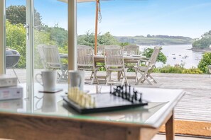A wooden deck with outdoor furniture, a chessboard, and a view of a lake and boats. - 4 Bed in Helford (oc-hclith) (Helford)