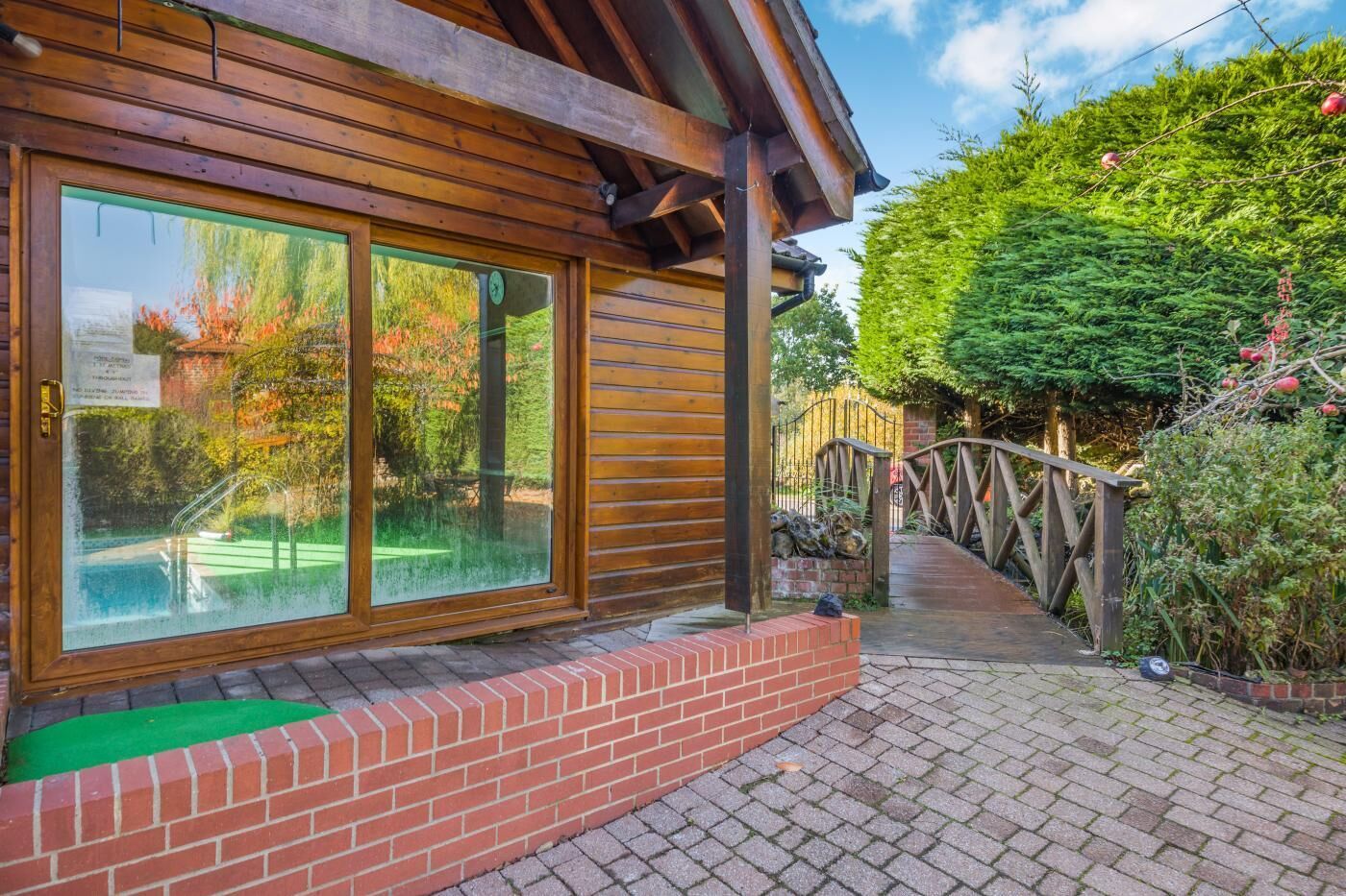 Un bâtiment en bois doté de grandes fenêtres, d’un chemin en briques et d’un pont en bois.