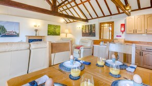 A dining area with a wooden table set for breakfast, a sofa, and a kitchen in the background. - 2 Bed in Smallburgh (oc-m33732) (Low Street)