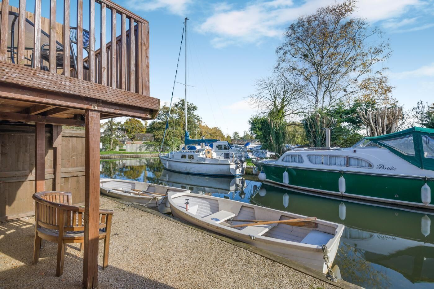 A wooden deck with a chair, a dock with boats, and a calm water body.