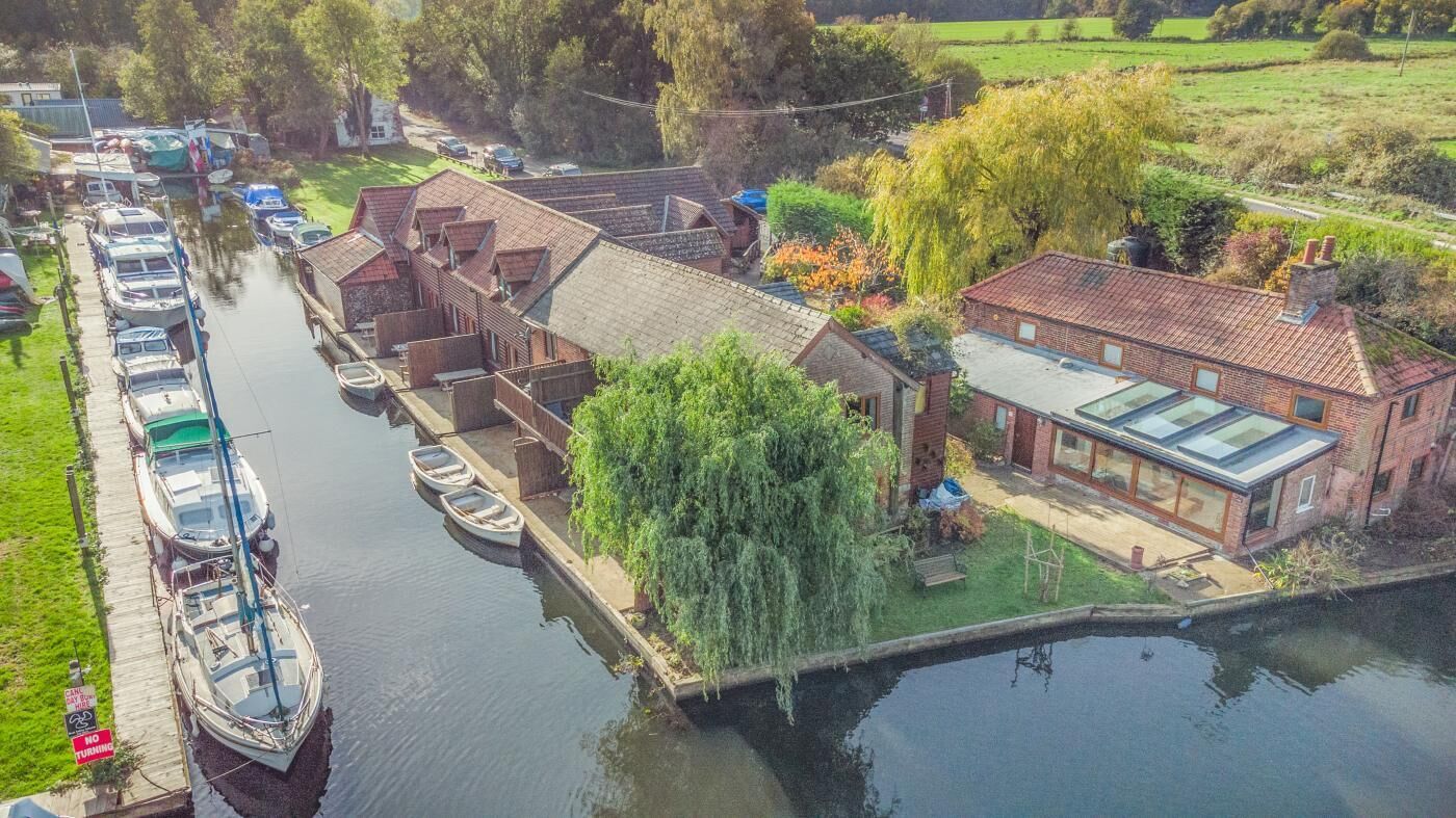 A riverside property with boats docked, a small garden, and a modern building with a glass roof.
