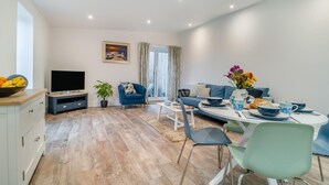 A modern living room with a TV, sofa, dining table, and chairs. - 2 Bed in Hinton Blewett (oc-g34070) (Hinton Blewett)