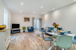 Ein modernes Wohnzimmer mit Fernseher, Sofa, Esstisch und Stühlen.