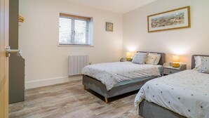 A bedroom with two beds, a radiator, a window with blinds, a framed picture on the wall, and a door. - 2 Bed in Hinton Blewett (oc-g34070) (Hinton Blewett)