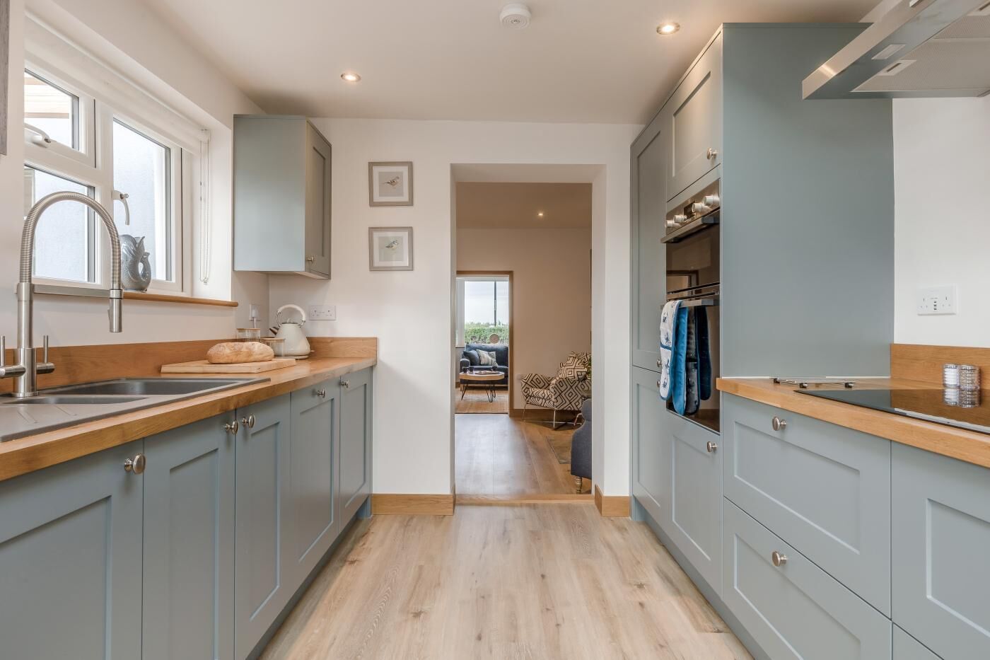 A modern kitchen with grey cabinets, a wooden countertop, and a view into a living area.