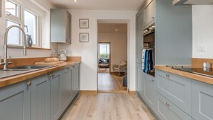 A modern kitchen with grey cabinets, a wooden countertop, and a view into a living area. - 4 Bed in Cromer (oc-b34005) (Cromer)