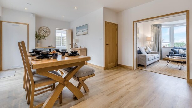 A modern living room with a wooden dining table, a sofa, and a view of the outdoors. - 4 Bed in Cromer (oc-b34005) (Cromer)