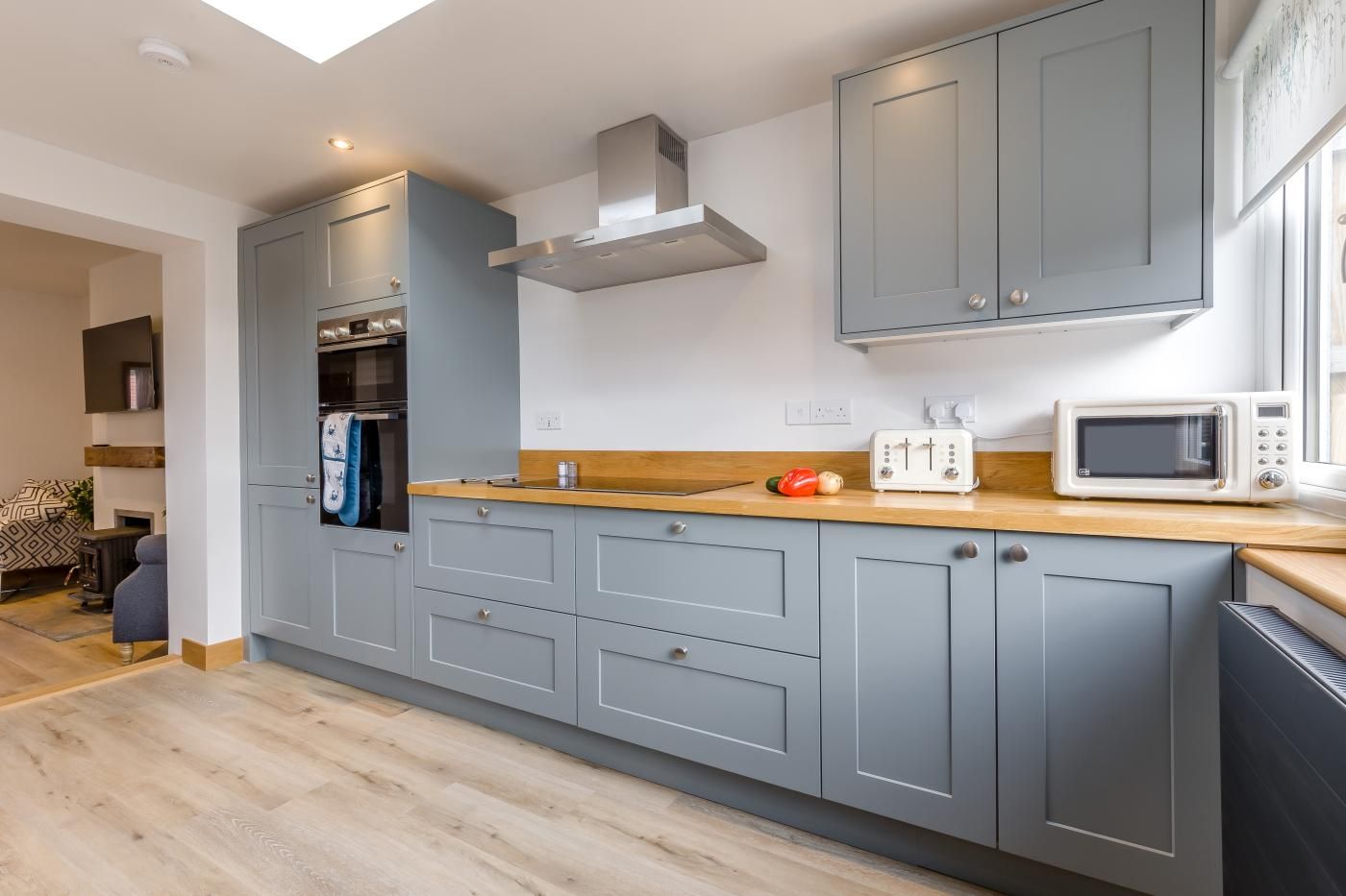 A modern kitchen with grey cabinets, a built-in oven, a microwave, and a wooden countertop.