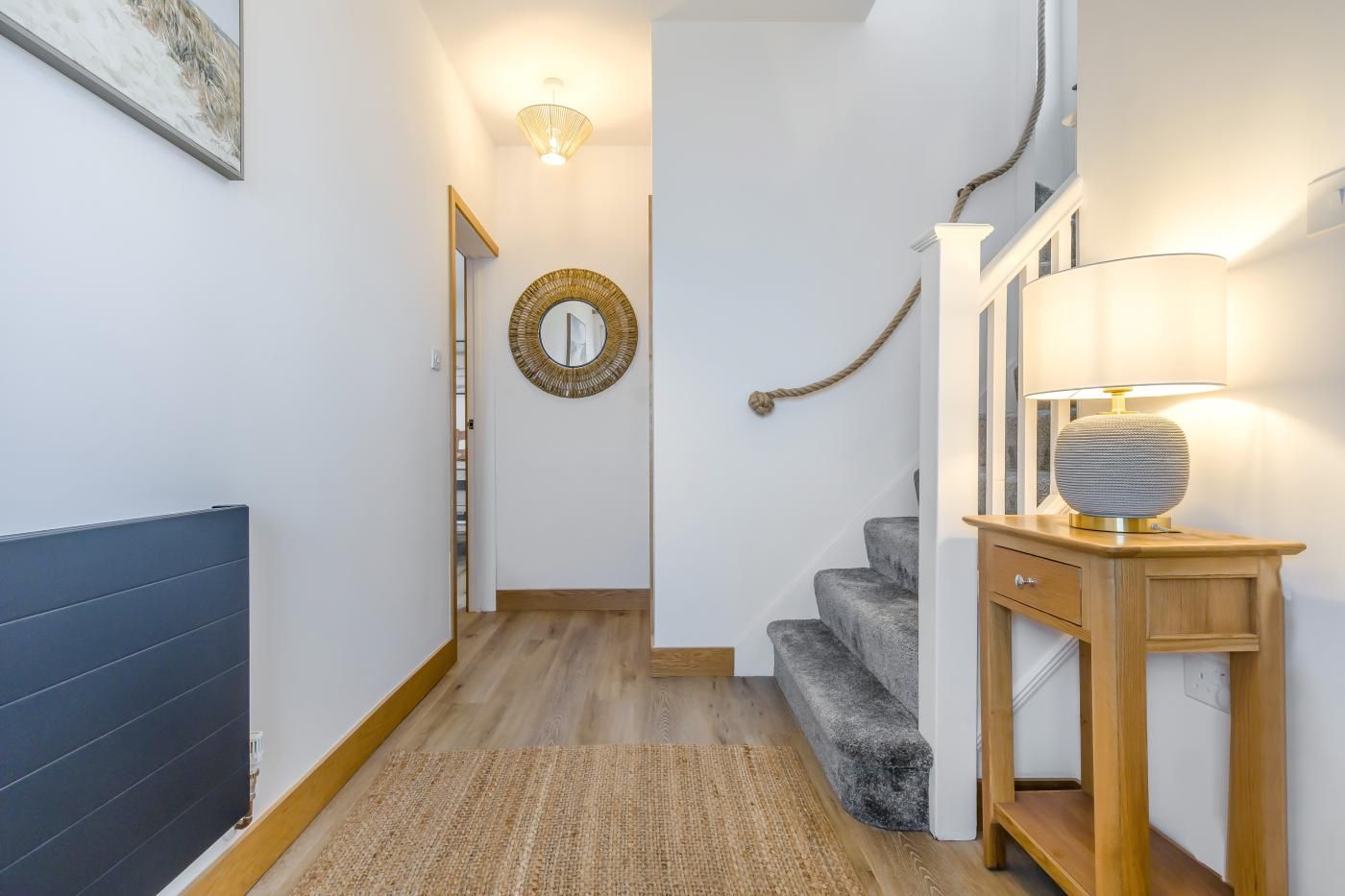 A hallway with a wooden floor, a mirror, a lamp, and a staircase.