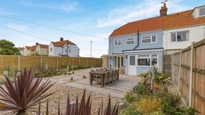 A two-story house with a wooden deck, a patio area, and a garden with various plants. - 4 Bed in Cromer (oc-b34005) (Cromer)