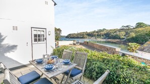 A table set with blue and white plates, a wooden chair, and a view of a harbor with boats and greenery. - 2 Bed in Helford (oc-hcpopi) (Helford)
