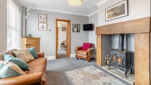 Ein gemütliches Wohnzimmer mit einer Ledersofa, einem Teppich mit Muster, einem Kamin und einem an der Wand befestigten Fernseher.