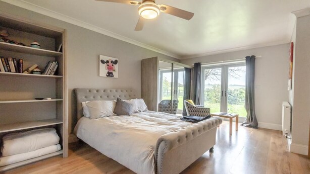 Ein Schlafzimmer mit einem Bett, einem Bücherregal, einem Deckenventilator und Blick ins Freie.