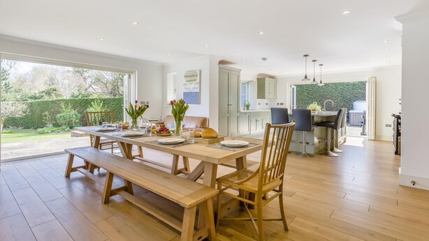 A spacious dining area with a wooden table and benches, a kitchen with modern appliances, and a view of the garden. - 5 Bed in Walberswick (oc-hlwal) (Walberswick)