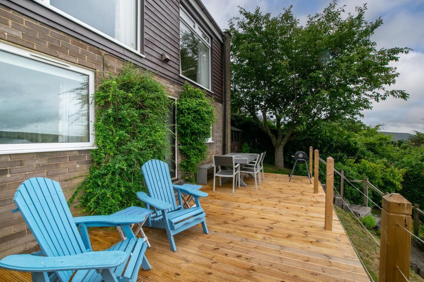 A deck with two blue Adirondack chairs, a wooden table, and a grill.