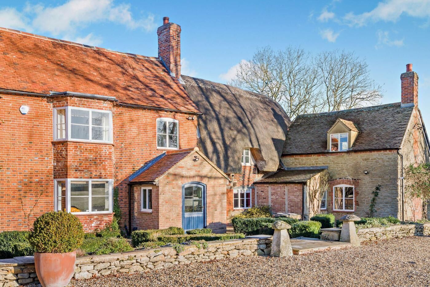 A traditional brick house with a thatched roof, a stone pathway, and a well-maintained garden.